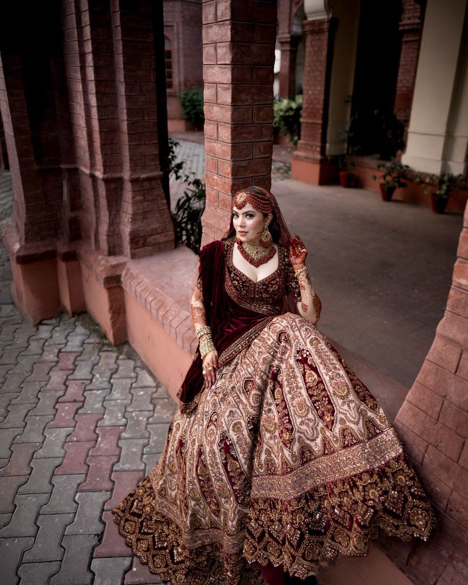 Bride seated on a brick ledge in the colonnade, her maroon and gold lehenga spread out, Adam & Sobia's wedding at Chamba House, Lahore