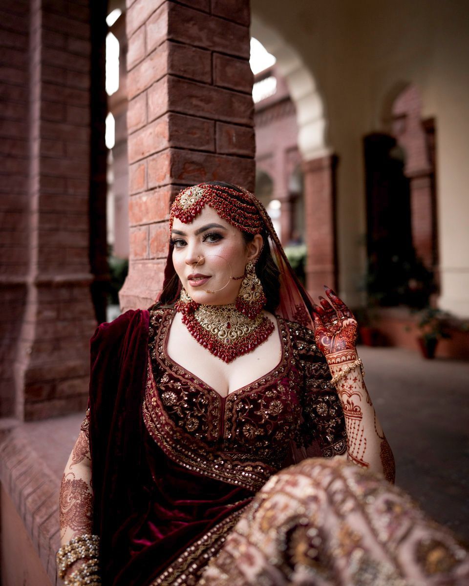 Close-up bridal portrait in the colonnade, wearing a red matha patti, layered necklace, and henna detail visible, Adam & Sobia's wedding at Chamba House, Lahore