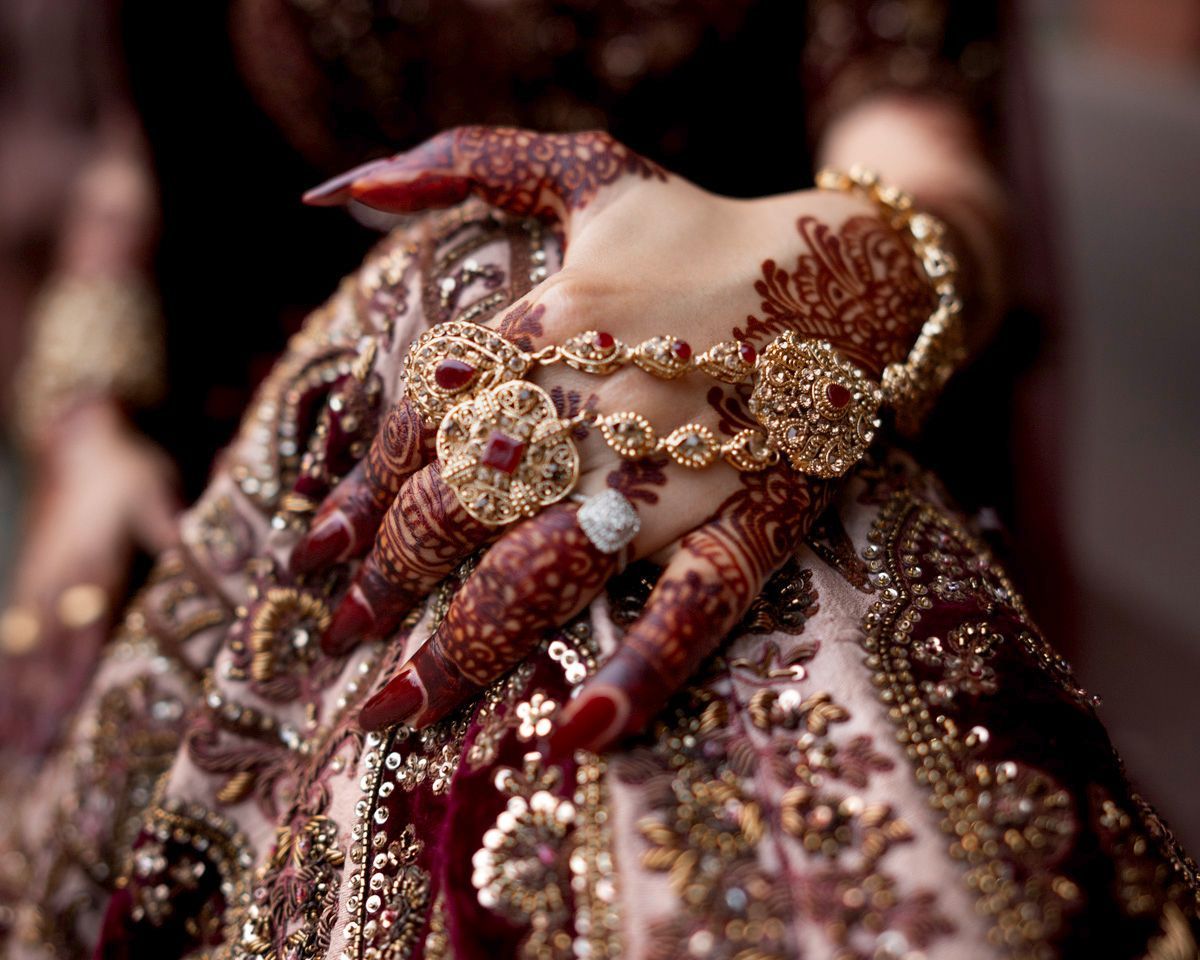 Detail of the bride's henna-painted hand resting on her embellished maroon lehenga, Adam & Sobia's wedding at Chamba House, Lahore