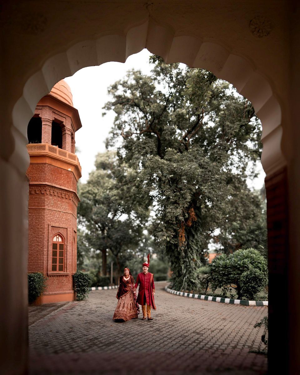 Bride and groom walking together down a brick path framed by a scalloped archway, Adam & Sobia's wedding at Chamba House, Lahore
