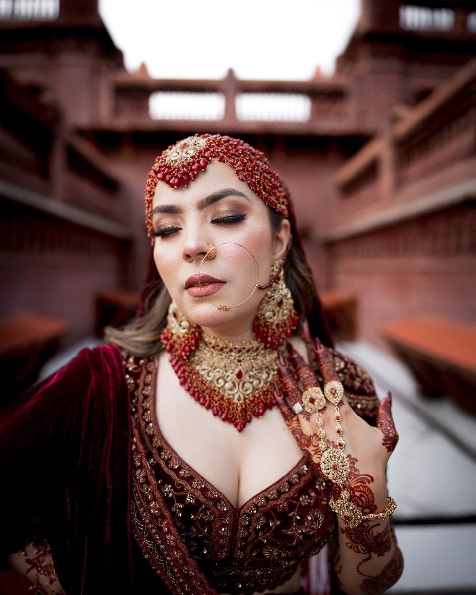 Close-up bridal portrait with eyes closed, wearing a red matha patti and layered choker, brick towers behind her, Adam & Sobia's wedding at Chamba House, Lahore