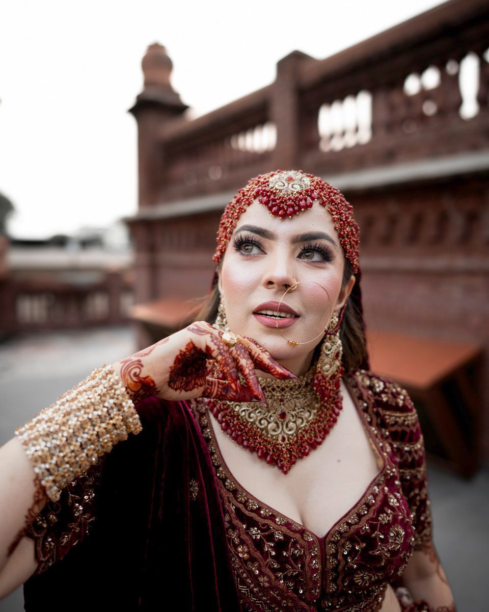 Close-up bridal portrait with hand near her chin, wearing a red matha patti and choker, Adam & Sobia's wedding at Chamba House, Lahore