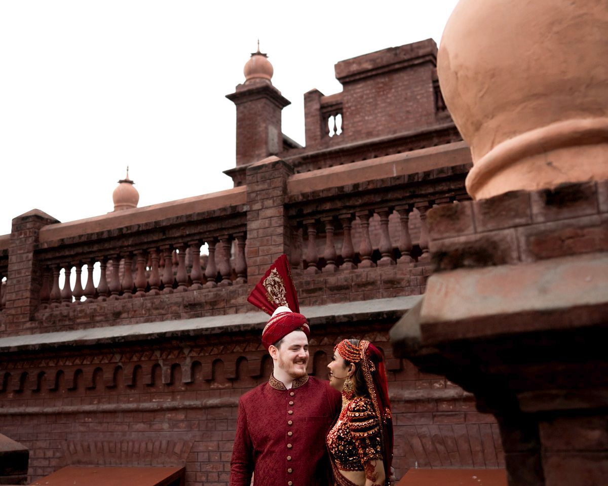 Bride and groom smiling at each other beneath brick domed towers, low-angle shot, Adam & Sobia's wedding at Chamba House, Lahore