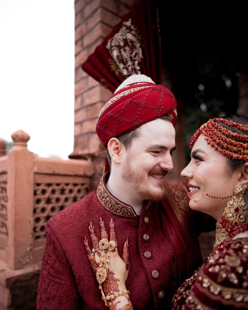 Close-up of bride and groom smiling at each other, her hand on his chest, brick balustrade behind them, Adam & Sobia's wedding at Chamba House, Lahore