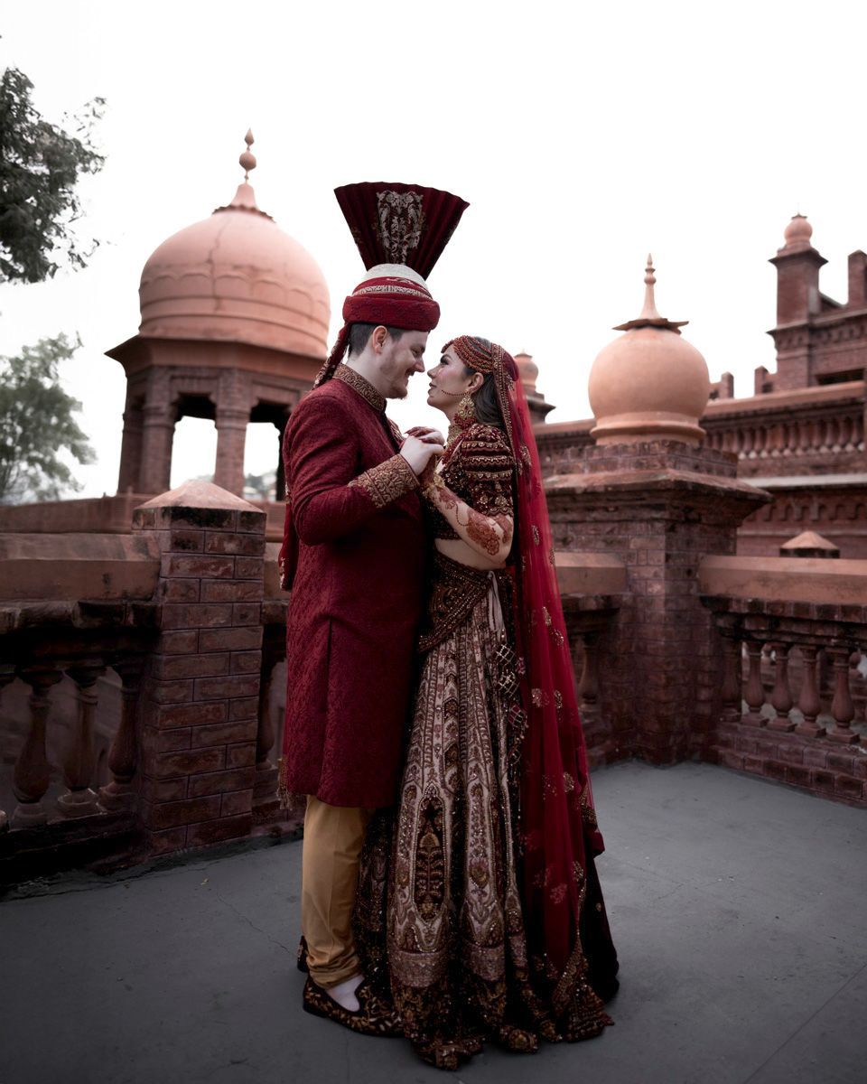 Bride and groom standing close together with domed brick towers in the background, Adam & Sobia's wedding at Chamba House, Lahore