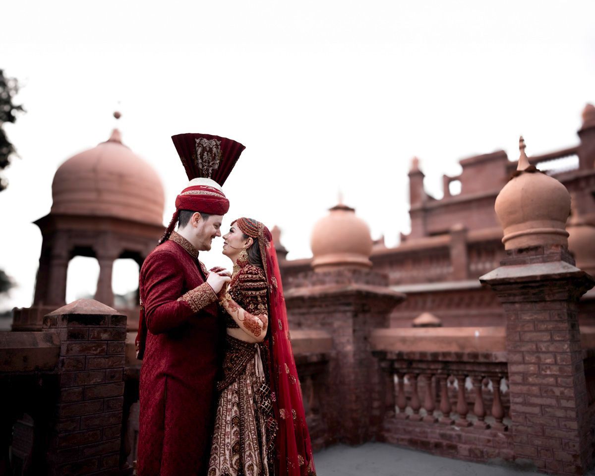 Bride and groom standing close together, profile view, with the brick fort facade behind them, Adam & Sobia's wedding at Chamba House, Lahore