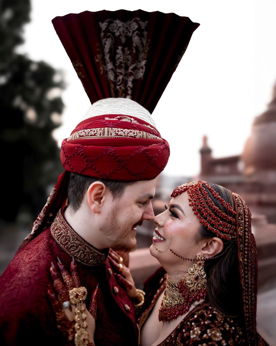 Close-up of bride and groom touching noses and smiling, brick towers softly blurred behind, Adam & Sobia's wedding at Chamba House, Lahore