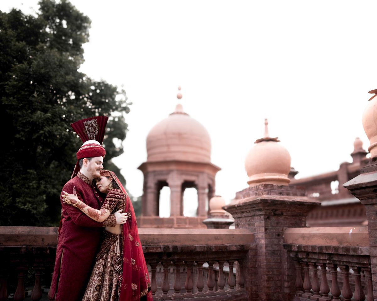 Bride and groom embracing tenderly with eyes closed, domed brick towers behind them, Adam & Sobia's wedding at Chamba House, Lahore