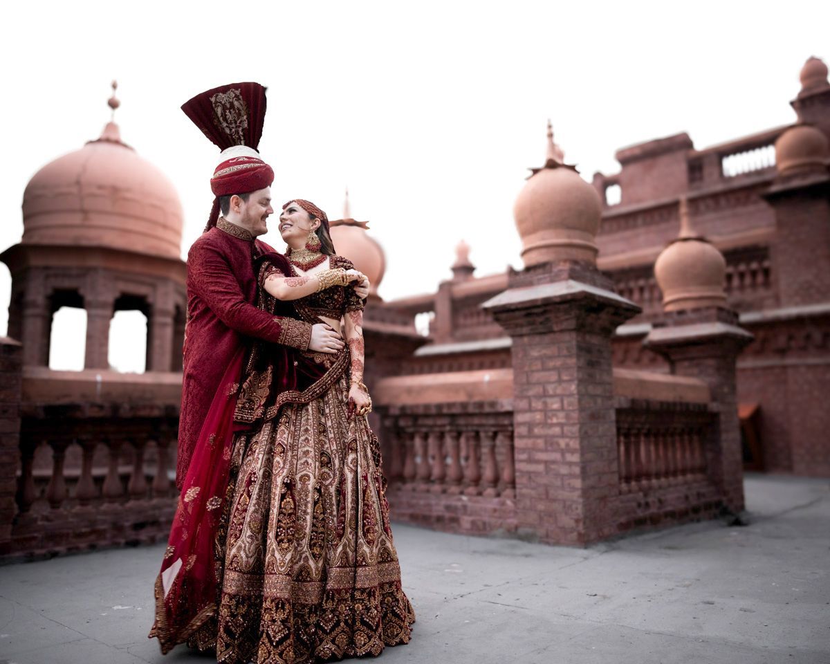 Bride and groom embracing and smiling, brick fort towers and balustrades behind them, Adam & Sobia's wedding at Chamba House, Lahore