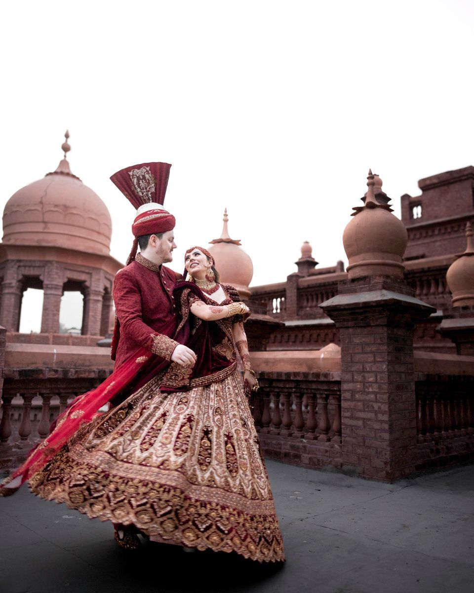 Bride's lehenga caught mid-twirl as she and the groom share a laugh, brick towers behind them, Adam & Sobia's wedding at Chamba House, Lahore