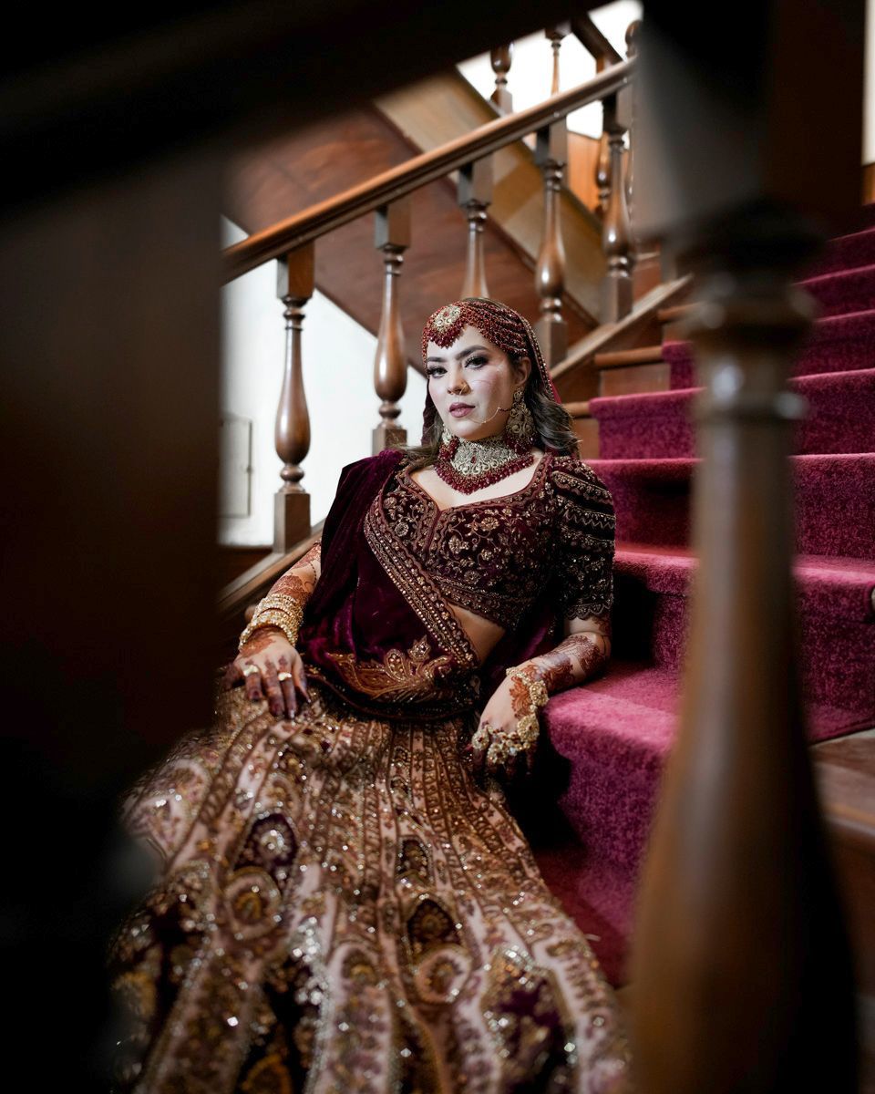 Solo bridal portrait seated on an indoor staircase with a maroon runner, Adam & Sobia's wedding