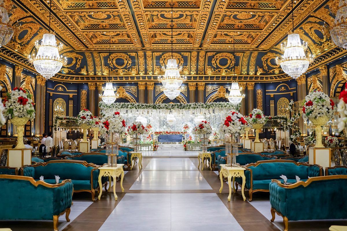 Wide shot of the empty reception ballroom decorated with gold detailing, chandeliers, and red and white floral arrangements, Adam & Sobia's wedding