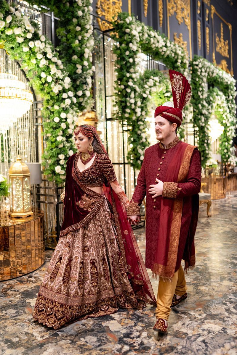 Bride and groom walking hand in hand into the reception venue, framed by hanging floral installations and gold-paneled walls, Adam & Sobia's wedding