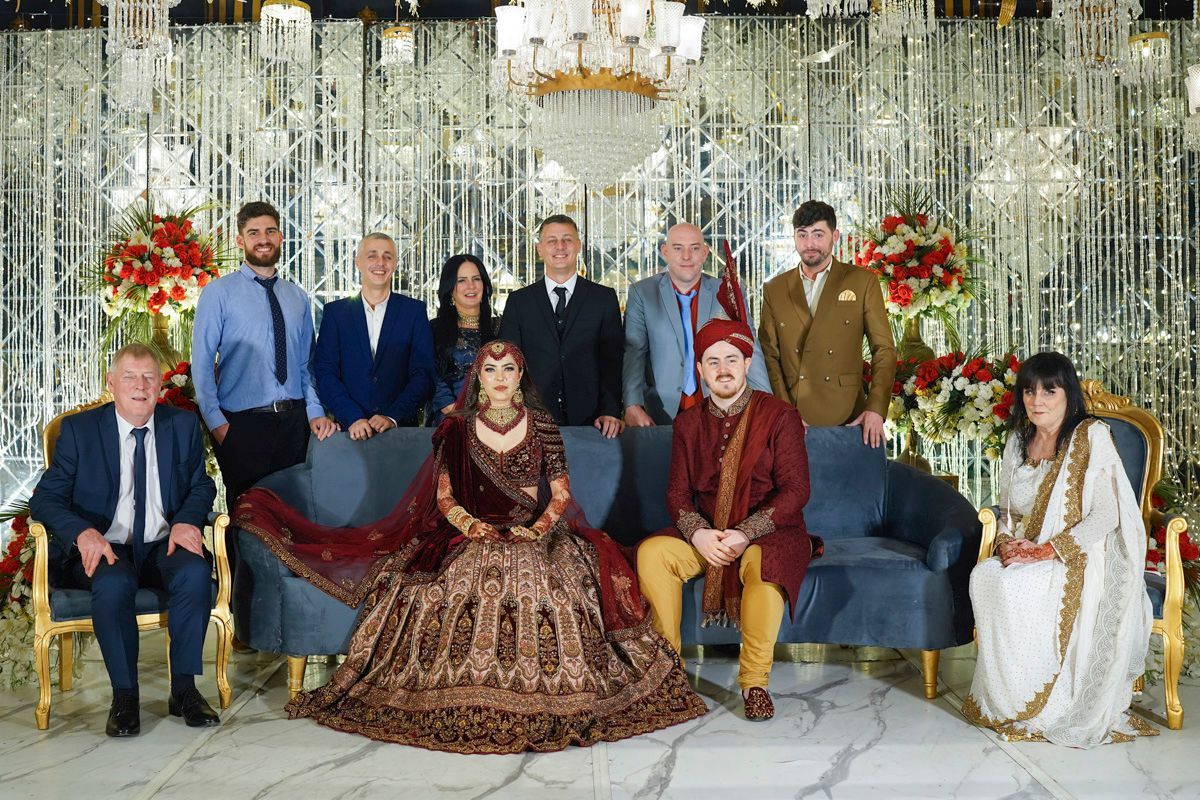 Extended family group portrait of bride, groom, and groom's relatives seated and standing on the reception stage, Adam & Sobia's wedding
