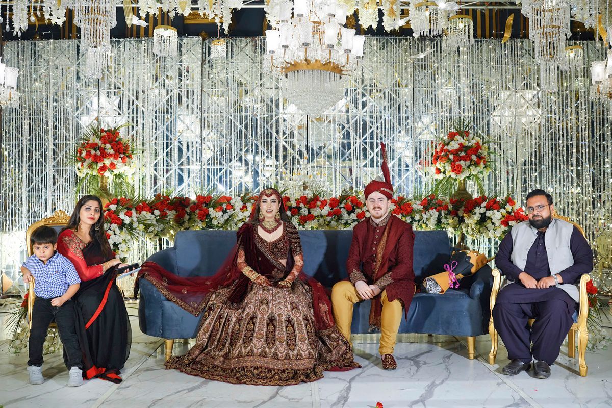Bride and groom seated on the reception stage sofa with family members on either side, Adam & Sobia's wedding