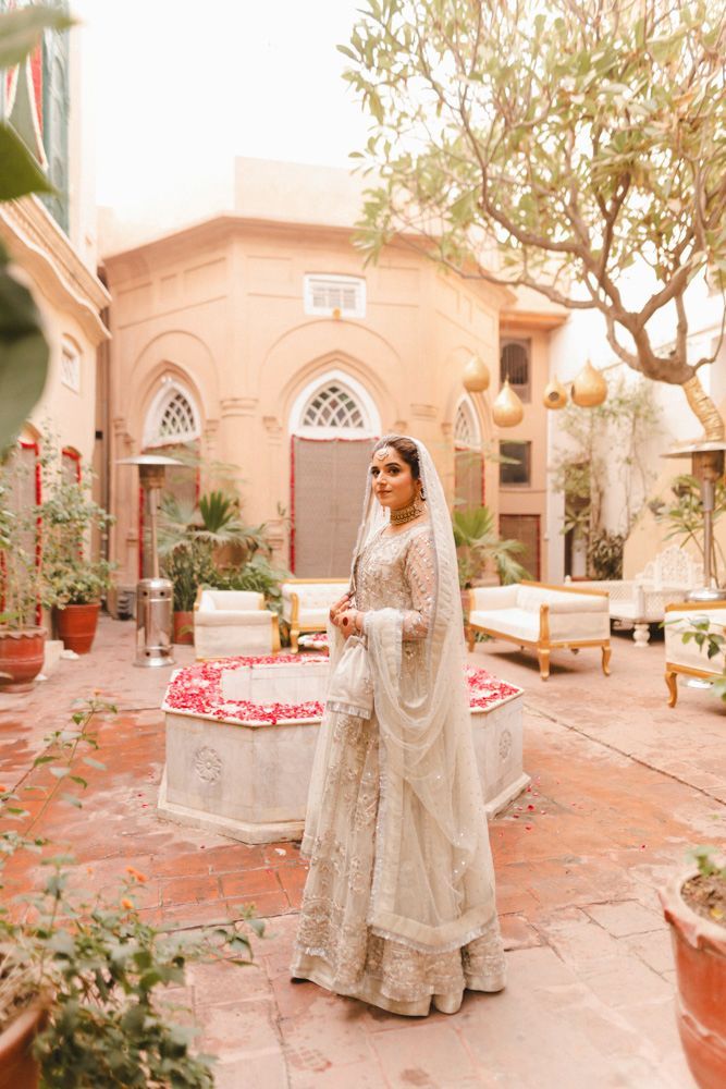 Solo bridal portrait standing beside the haveli's marble fountain filled with rose petals, Ahmed & Laraib's wedding at Barood Khana Haveli, Lahore