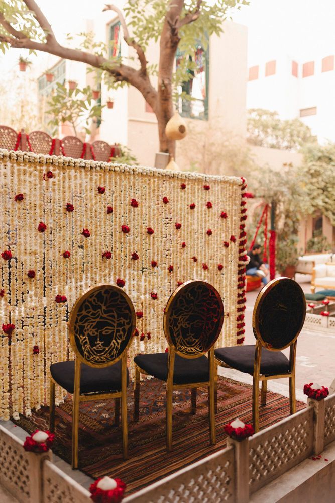 Detail of three gold chairs with Medusa-motif backs set on a patterned rug before the floral curtain, Ahmed & Laraib's wedding at Barood Khana Haveli, Lahore