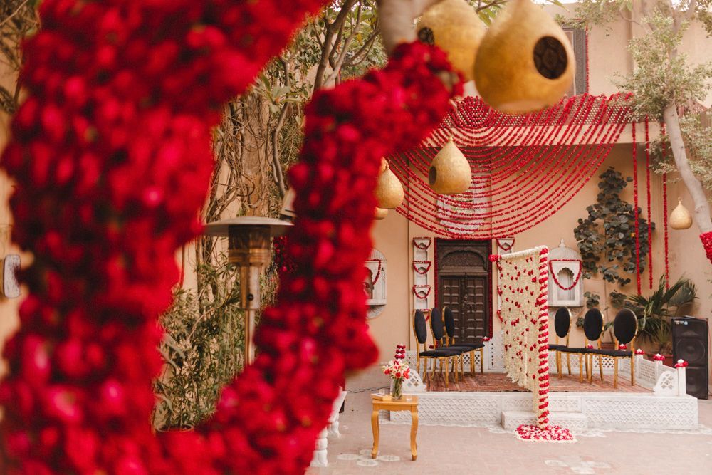 Decor detail of the haveli courtyard viewed through hanging red floral strands, Ahmed & Laraib's wedding at Barood Khana Haveli, Lahore