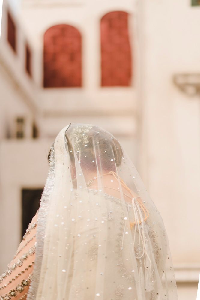 Bride viewed from behind beneath her sparkling veil, heritage architecture blurred behind her, Ahmed & Laraib's wedding