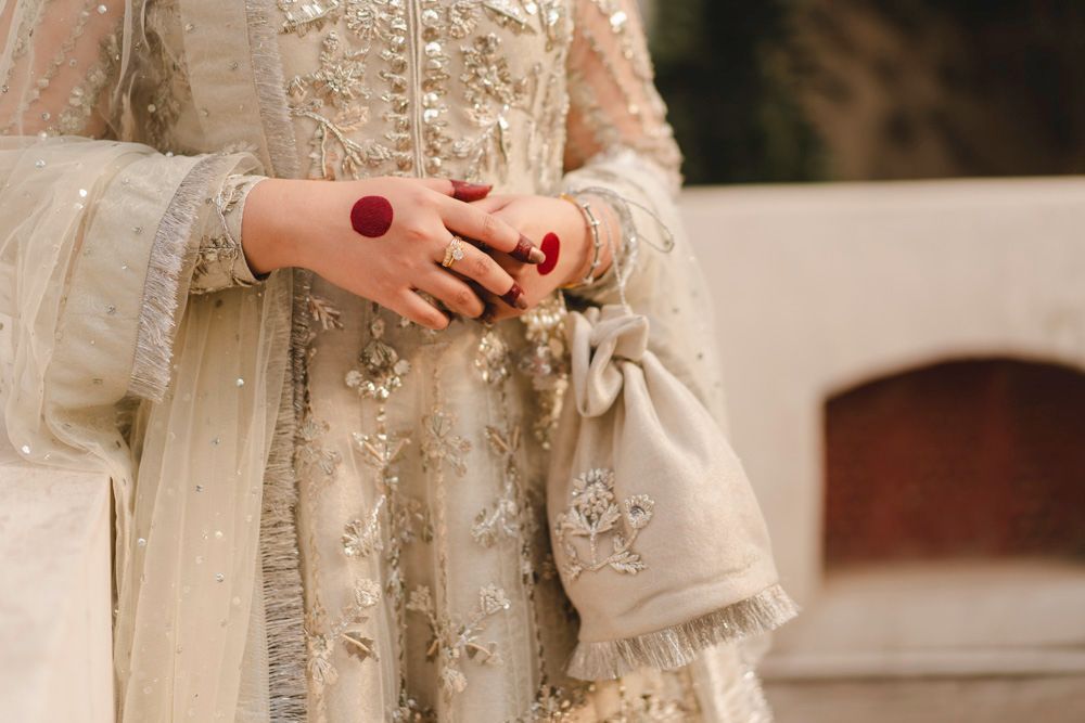 Detail of the bride's hennaed hand and embellished outfit, holding a beaded clutch, Ahmed & Laraib's wedding