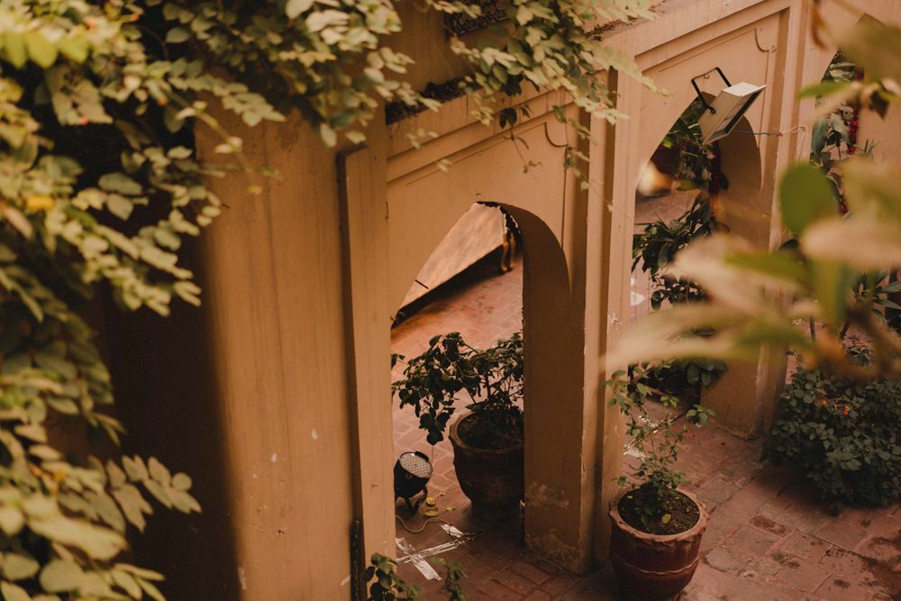 View through a haveli archway toward a covered courtyard corner with potted plants, Ahmed & Laraib's wedding at Barood Khana Haveli, Lahore