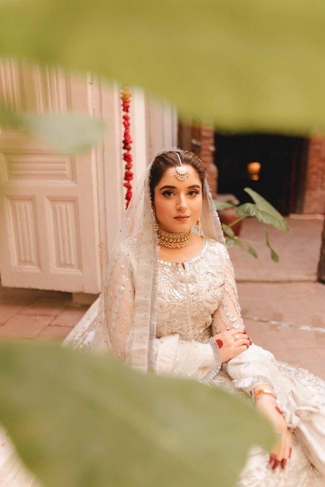 Solo bridal portrait seated in the haveli courtyard, framed by green leaves in the foreground, Ahmed & Laraib's wedding