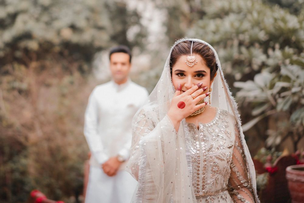 Bride covering her mouth and laughing, groom in a white sherwani blurred behind her, Ahmed & Laraib's wedding