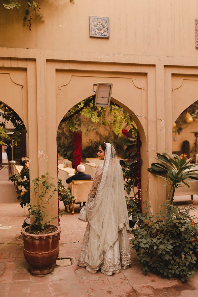 Bride viewed from behind walking through a haveli archway toward the seating area, Ahmed & Laraib's wedding