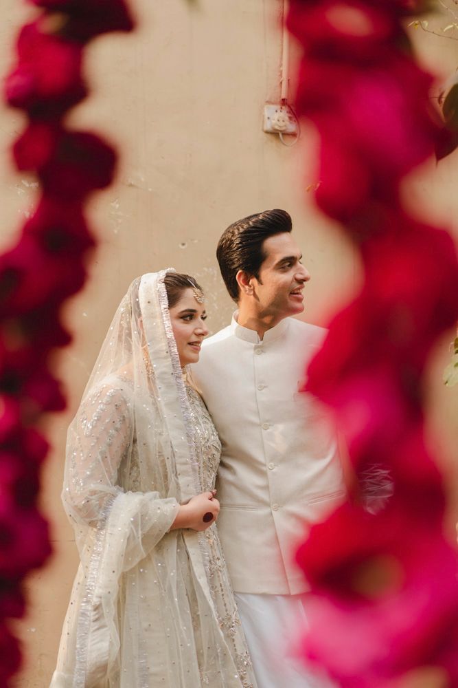 Bride and groom smiling at each other, framed by hanging red floral garlands, Ahmed & Laraib's wedding