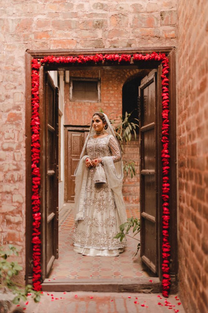 Solo bridal portrait standing in a flower-framed doorway at the haveli, Ahmed & Laraib's wedding at Barood Khana Haveli, Lahore