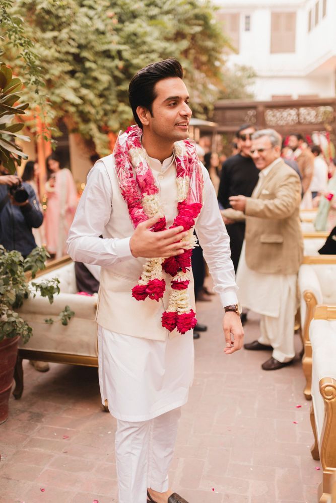 Groom walking through the haveli courtyard wearing a flower garland, guests gathered behind him, Ahmed & Laraib's wedding