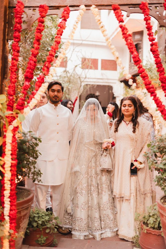 Bride's entrance procession beneath a floral garland archway, escorted by family, Ahmed & Laraib's wedding at Barood Khana Haveli, Lahore