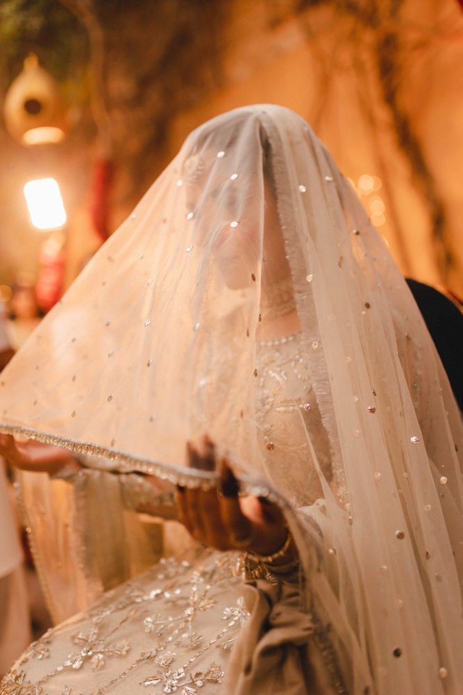 Close-up of the bride beneath her sequined veil at night, golden light glowing behind her, Ahmed & Laraib's wedding