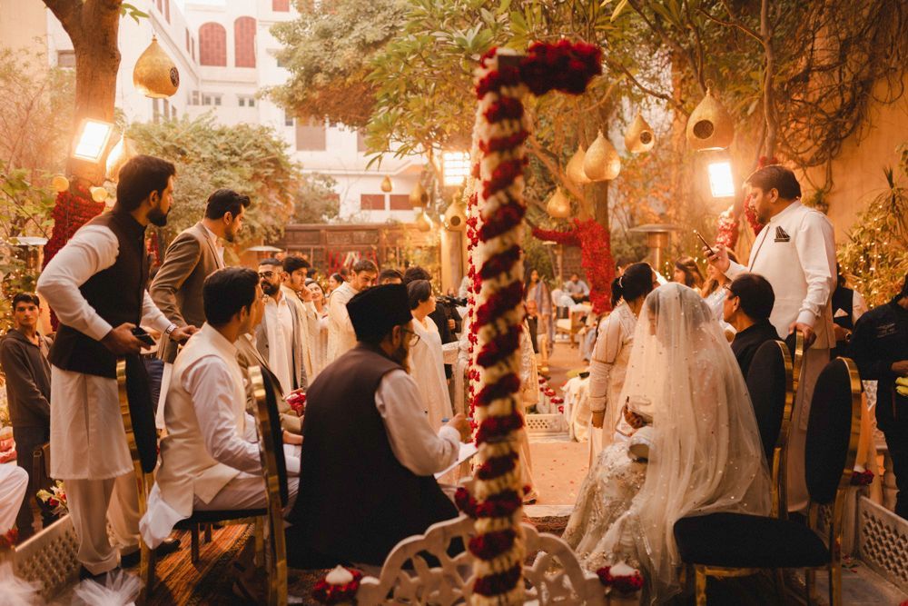 Wide shot of the nikah ceremony in the haveli courtyard, bride and groom seated facing each other, guests gathered around, Ahmed & Laraib's wedding at Barood Khana Haveli, Lahore