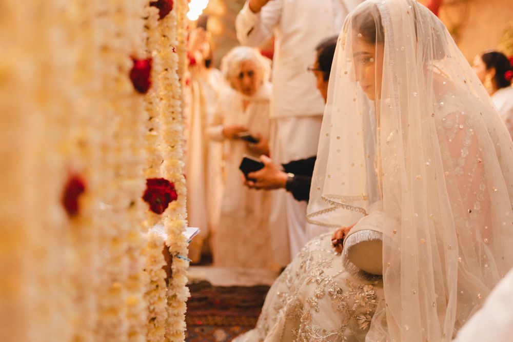 Bride seated beneath her veil during the nikah as a family member holds up a phone nearby, Ahmed & Laraib's wedding