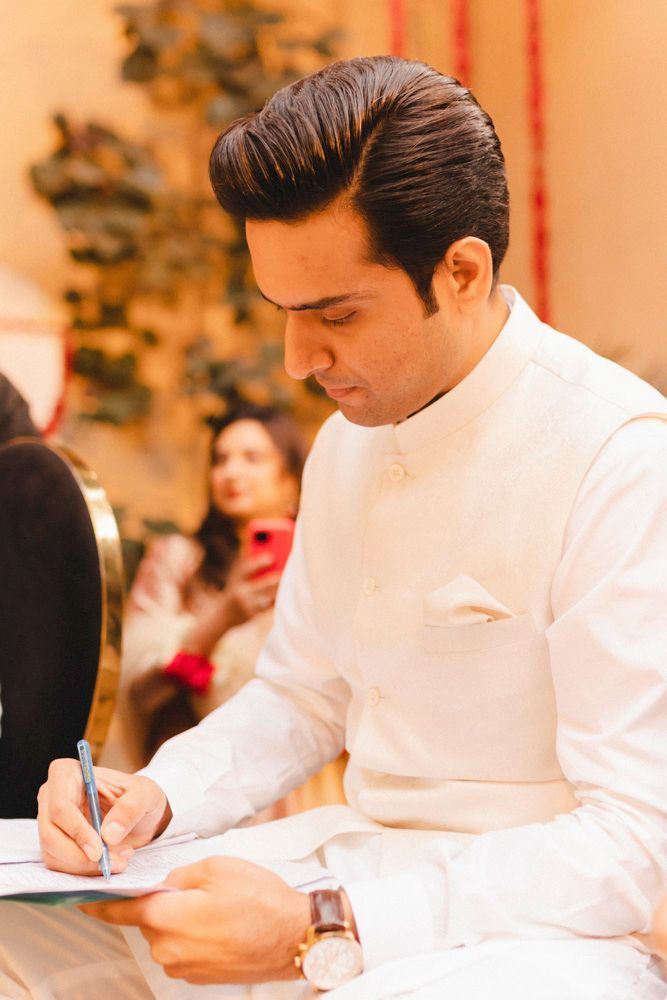Close-up of the groom signing the nikah register, a guest taking a photo in the background, Ahmed & Laraib's wedding
