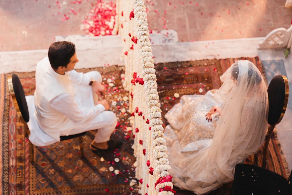 Overhead view of bride and groom seated for the nikah, separated by the red and white floral pillar, Ahmed & Laraib's wedding at Barood Khana Haveli, Lahore