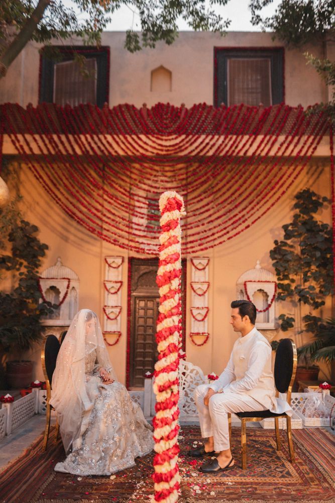 Wide shot of bride and groom seated for their nikah ceremony beneath red and white garland draping, Ahmed & Laraib's wedding at Barood Khana Haveli, Lahore