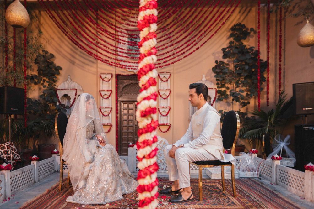 Bride and groom seated facing each other for the nikah, marigold garland pillar between them, Ahmed & Laraib's wedding at Barood Khana Haveli, Lahore