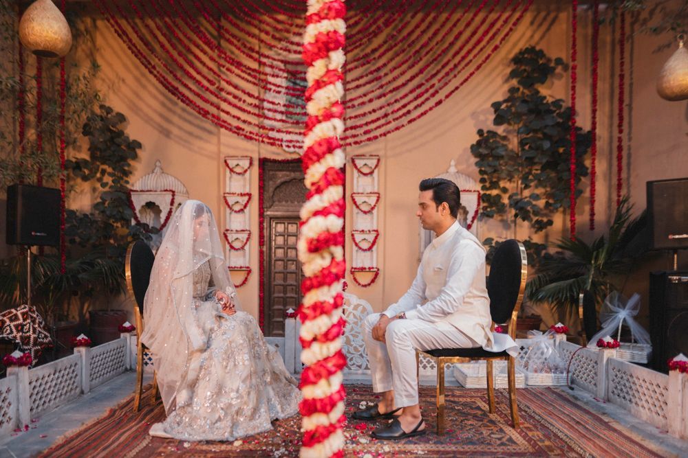 Bride and groom seated for the nikah ceremony in the haveli courtyard, wide shot with garland draping overhead, Ahmed & Laraib's wedding