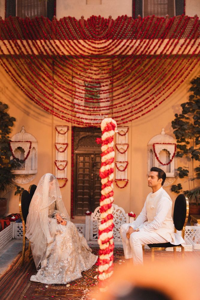 Bride and groom seated for the nikah, viewed from a slight distance beneath the floral canopy, Ahmed & Laraib's wedding at Barood Khana Haveli, Lahore