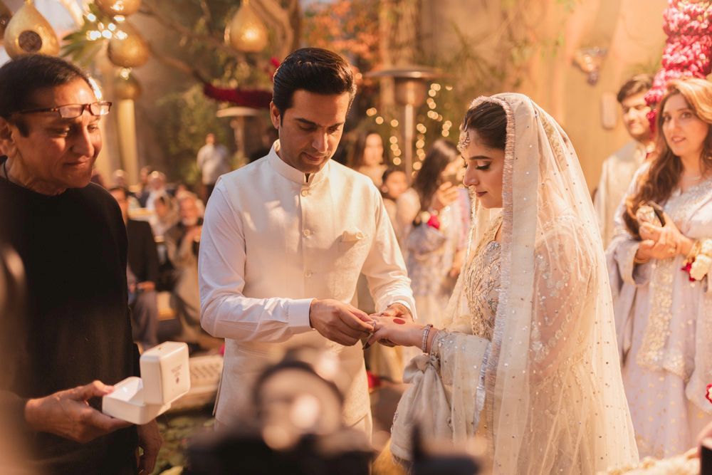 Groom placing a ring on the bride's finger as family look on, Ahmed & Laraib's wedding
