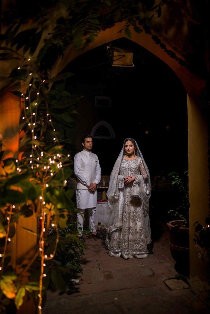 Bride and groom standing together at night, framed by a haveli archway and fairy lights, Ahmed & Laraib's wedding