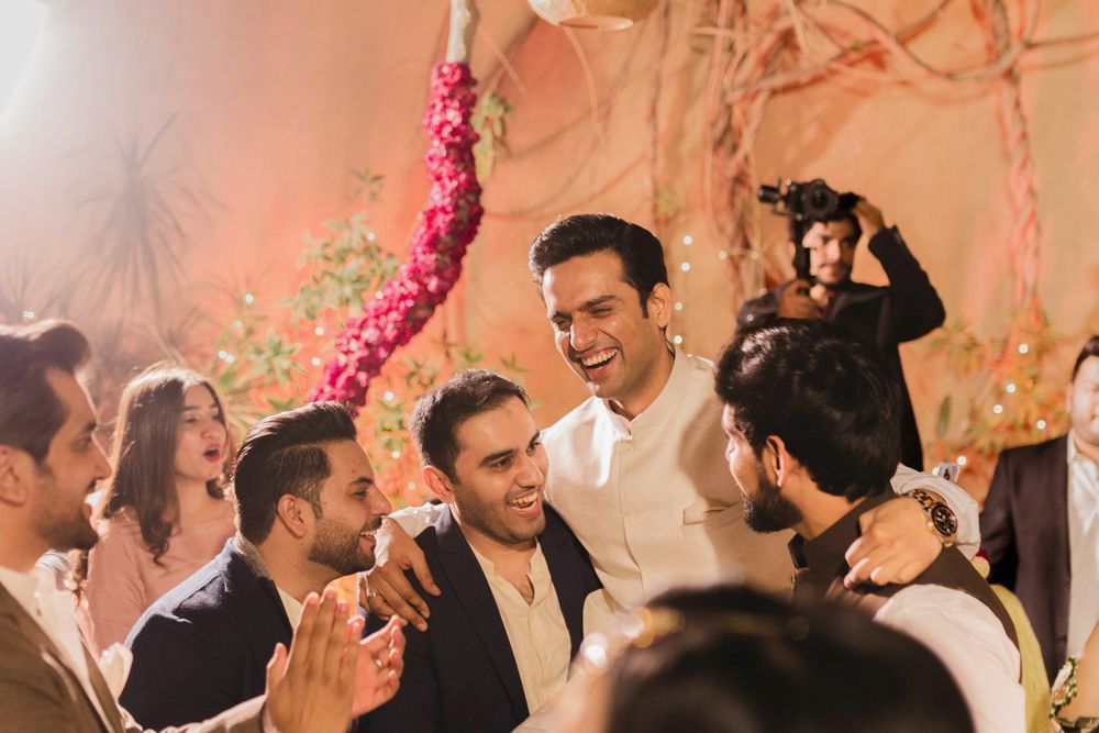Groom laughing with a group of friends at the night celebration, a videographer filming behind them, Ahmed & Laraib's wedding