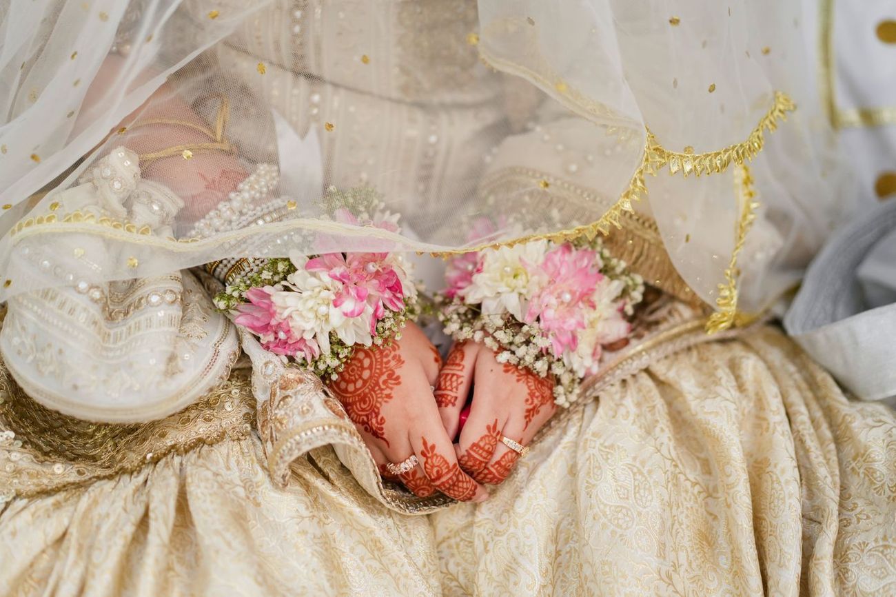 Detail of the bride's henna-painted hands resting on her lap, holding pink and white flowers, Maham & Aurangzeb's wedding