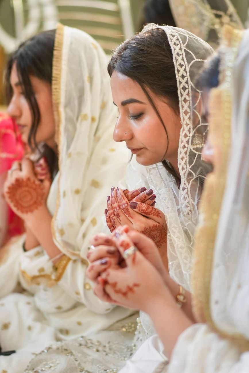 Women raising their palms in prayer during the nikah ceremony, henna visible on their hands, Maham & Aurangzeb's wedding