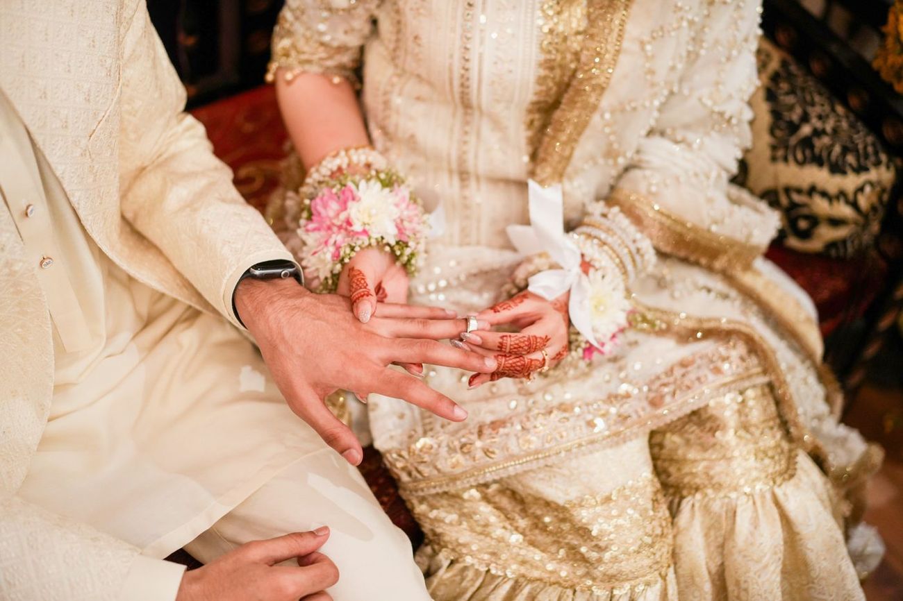 Detail of bride and groom's joined hands with the wedding ring, her henna and floral wristlet visible, Maham & Aurangzeb's wedding