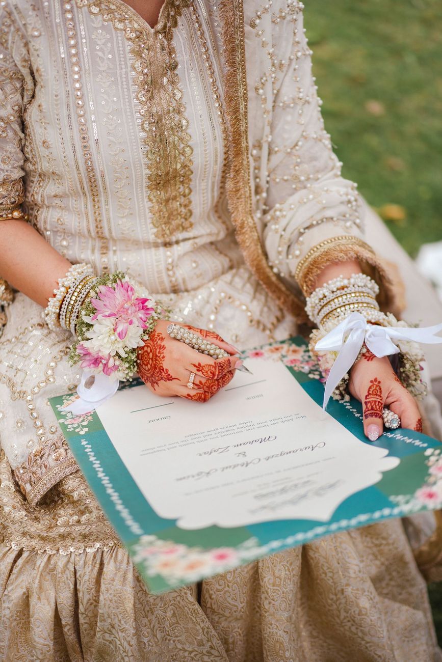 Detail of the bride's henna-painted hands holding the decorative nikah certificate, Maham & Aurangzeb's wedding