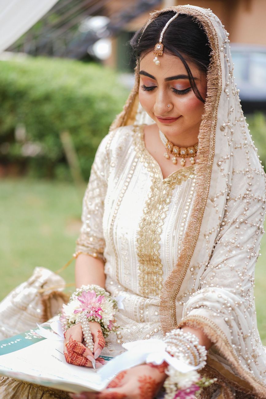 Bride signing the nikah certificate outdoors, floral wristlets visible on her hands, Maham & Aurangzeb's wedding