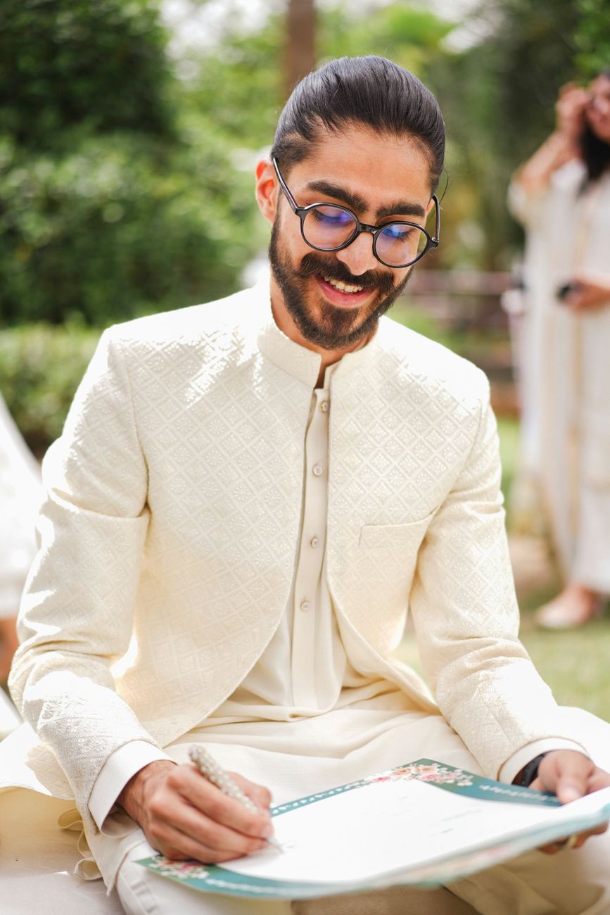 Solo groom portrait smiling while signing the nikah certificate outdoors, Maham & Aurangzeb's wedding